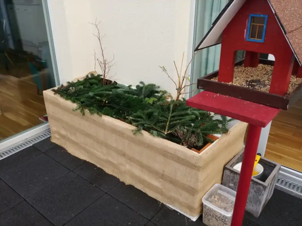 Pflanzen im Blumenkasten auf dem Balkon überwintern - Balkonkasten zum überwintern mit Jute, Styropor und Zweigen vorbereitet.